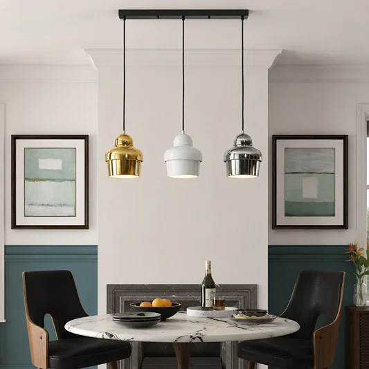 Three modern pendant lights in gold, white, and silver finishes hanging over a dining table in a styled interior room.