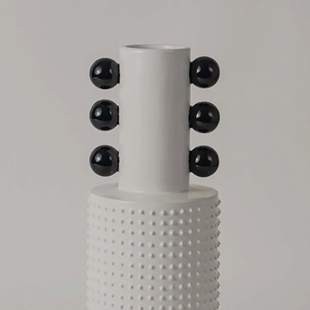 Closeup image of a white studded ceramic totem vase accented with rows of glossy black structural spheres on its neck.