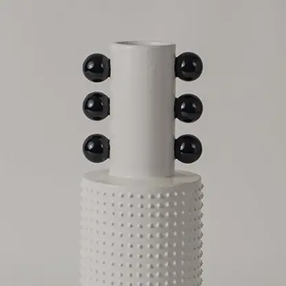 Closeup image of a white studded ceramic totem vase accented with rows of glossy black structural spheres on its neck.