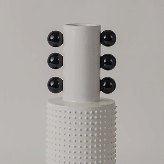 Closeup image of a white studded ceramic totem vase accented with rows of glossy black structural spheres on its neck.