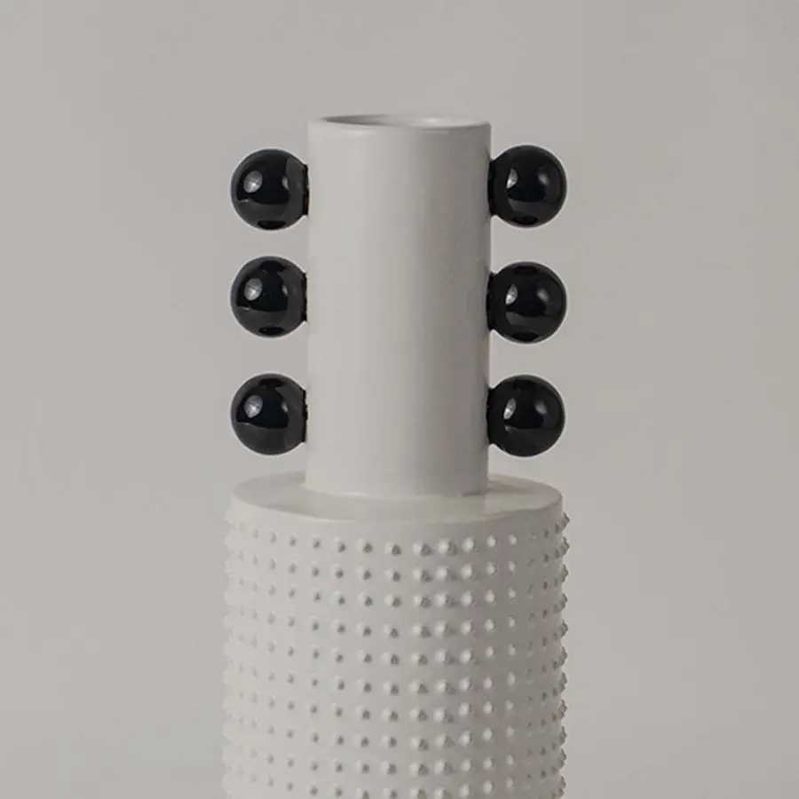 Closeup image of a white studded ceramic totem vase accented with rows of glossy black structural spheres on its neck.