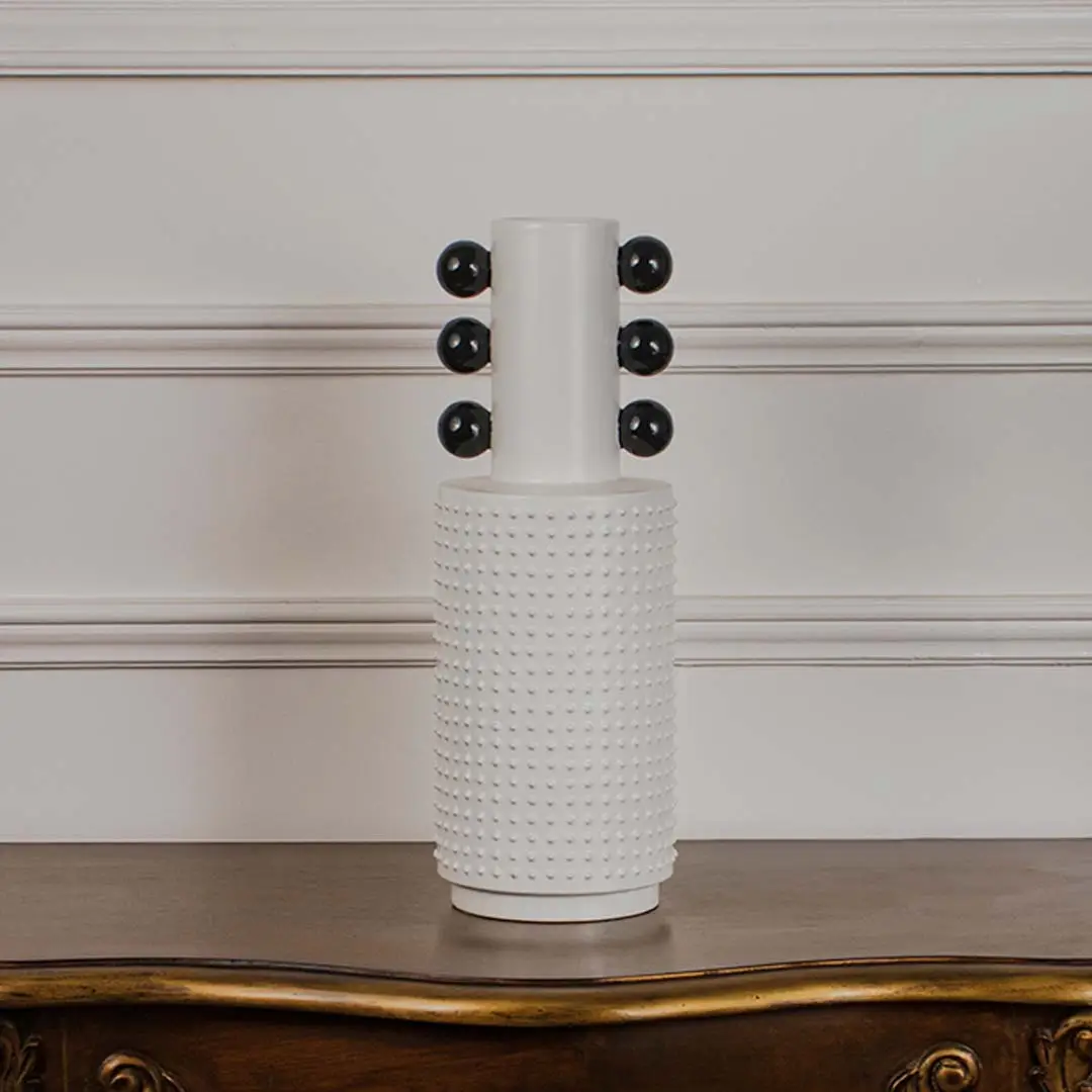 White studded ceramic totem vase with glossy black accent spheres displayed on a classic wooden console table for styling.