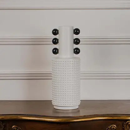 White studded ceramic totem vase with glossy black accent spheres displayed on a classic wooden console table for styling.