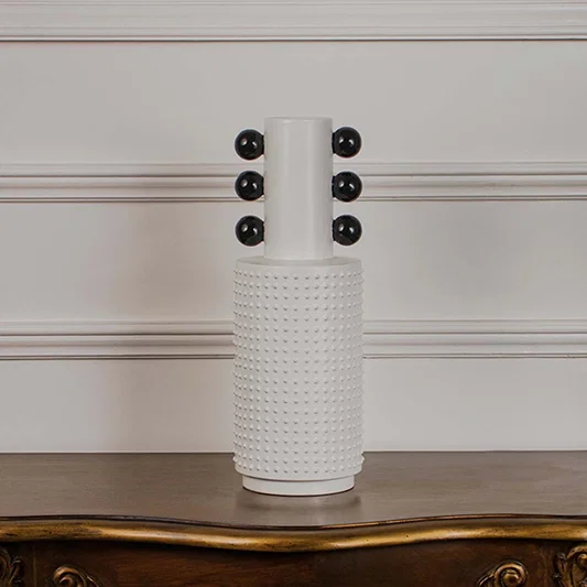 White studded ceramic totem vase with glossy black accent spheres displayed on a classic wooden console table for styling.