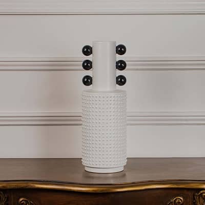 White studded ceramic totem vase with glossy black accent spheres displayed on a classic wooden console table for styling.