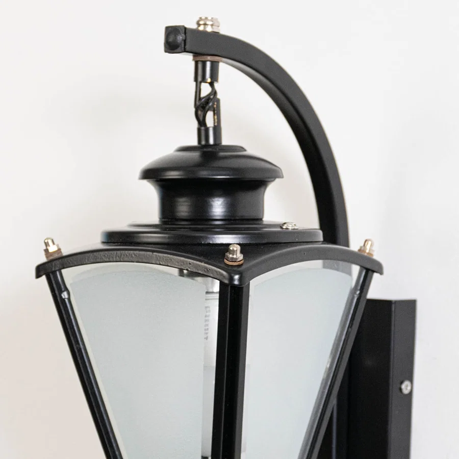 Closeup of black metal outdoor wall lantern with frosted glass panels showing textured finish sturdy build and classic detailing.