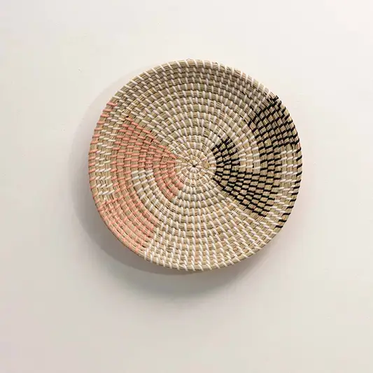 Round handcrafted natural seagrass wall basket with pink and black abstract color block patterns on white background.