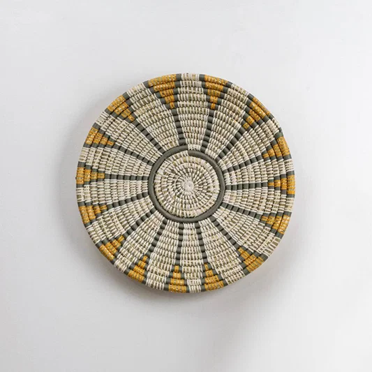 Round handcrafted seagrass wall basket with white grey and mustard pattern for home décor on white background image.