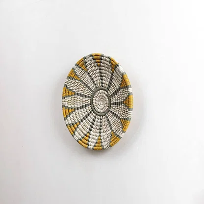Round handcrafted seagrass wall basket with white grey and mustard pattern for home décor on white background image.