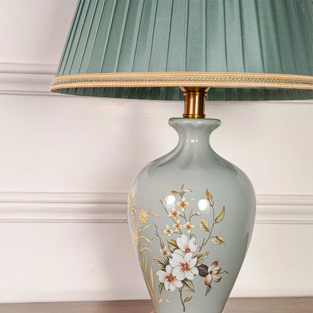 Closeup of sage green ceramic table lamp showing delicate hand painted floral details smooth glaze and gold metal base.