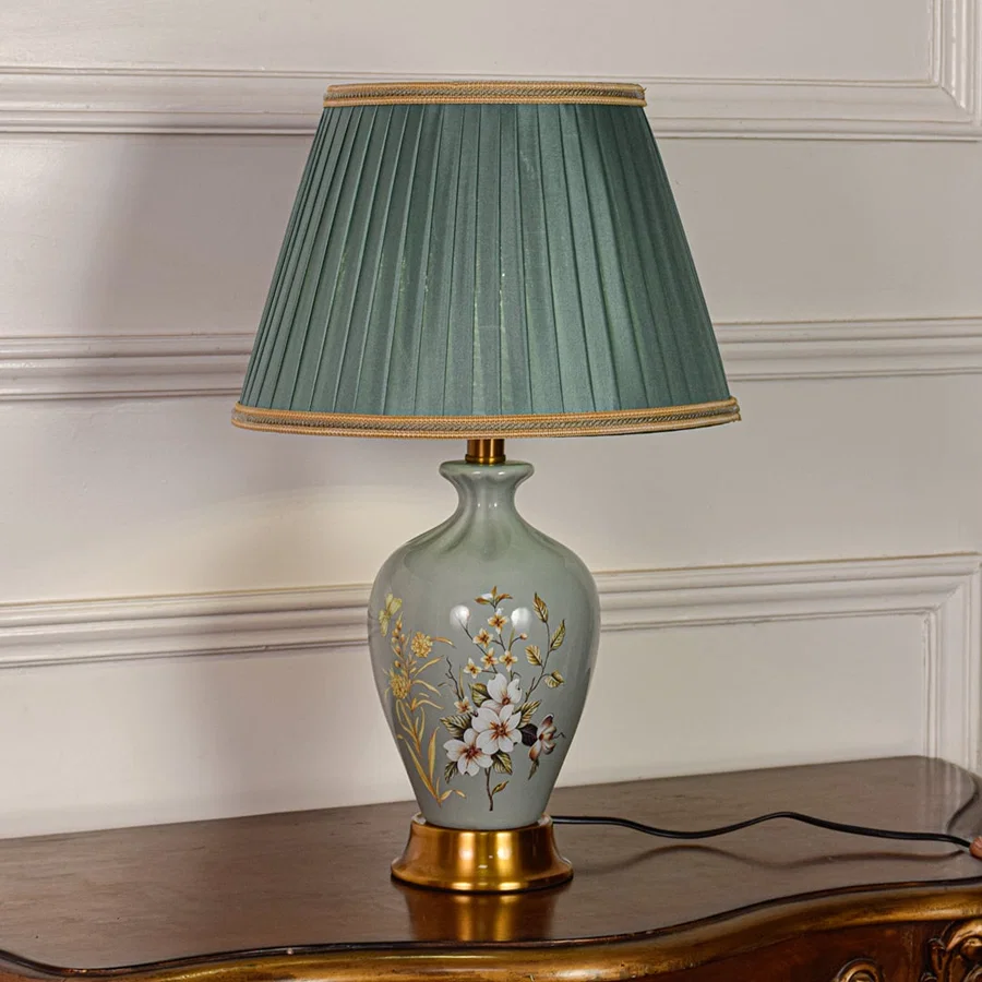 Sage green ceramic table lamp featuring floral detailing gold metal base and pleated fabric shade displayed on white background.