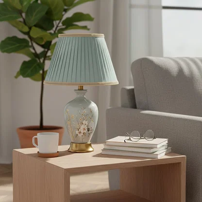 Sage green ceramic table lamp with hand painted floral artwork gold metal base and pleated fabric shade styled on side table.