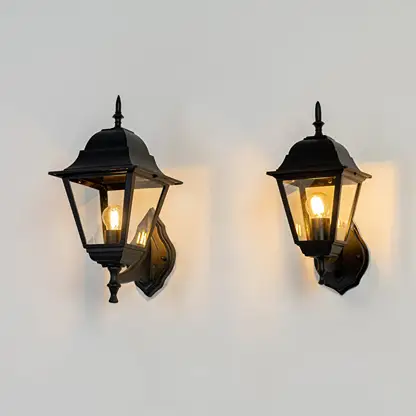 Black metal and glass outdoor wall lantern lights grouped on white background glowing warmly for porch entryway decor Light on white BG.