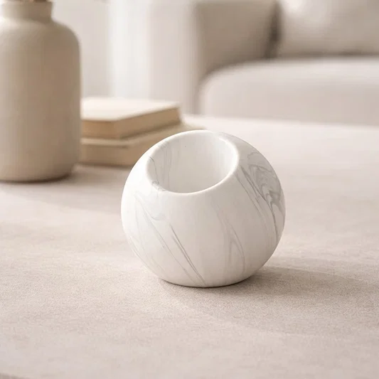 White marble finish ceramic round vase placed on tabletop in warm neutral living room styling setup.