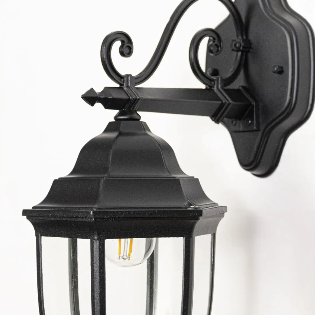 Closeup image of Victorian outdoor wall light facing downward in black metal highlighting ornate design glass shade and exterior wall use.