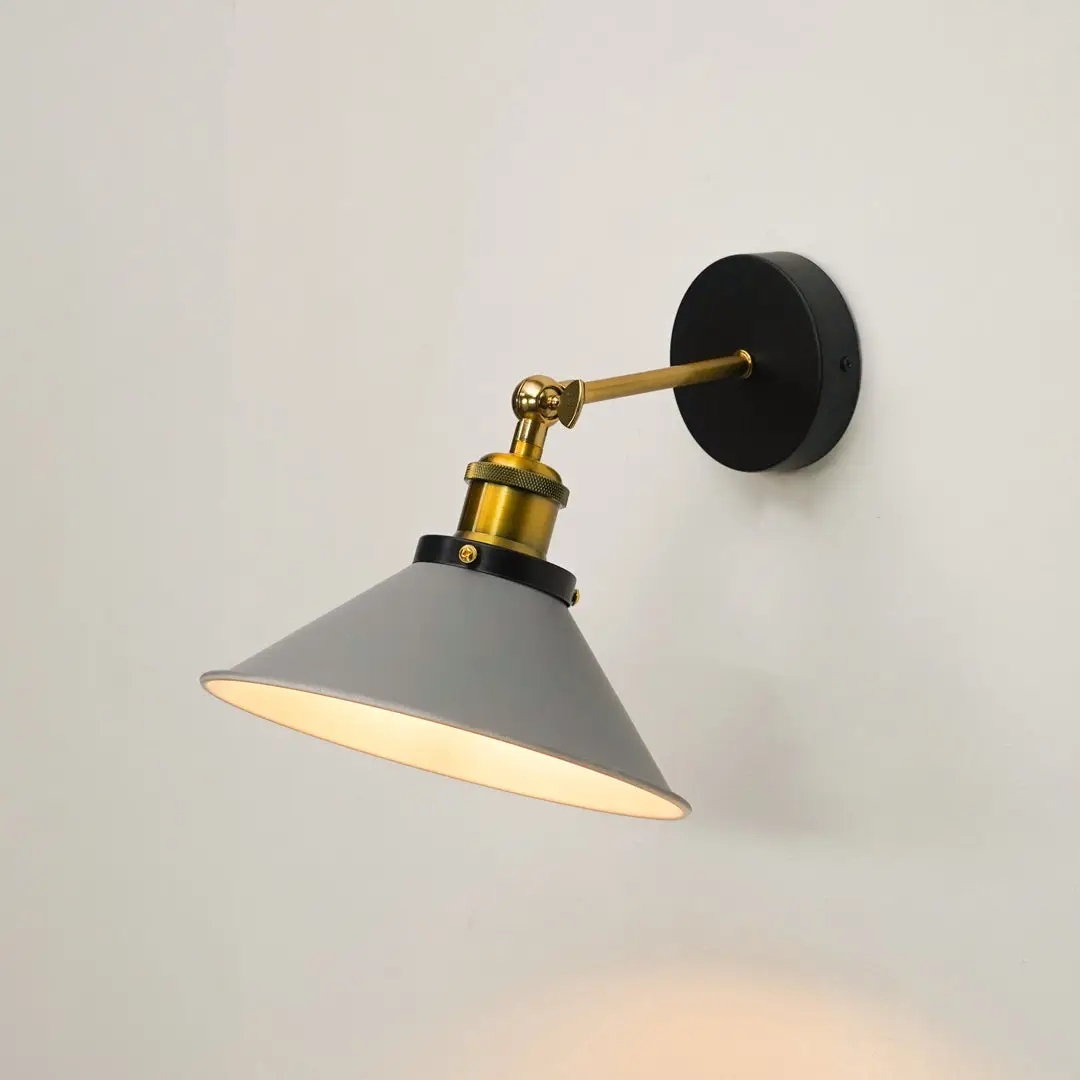 A modern wall-mounted sconce with a gray conical shade, gold-toned metal arm and collar, and a round black wall plate, shown lit against a plain light wall.