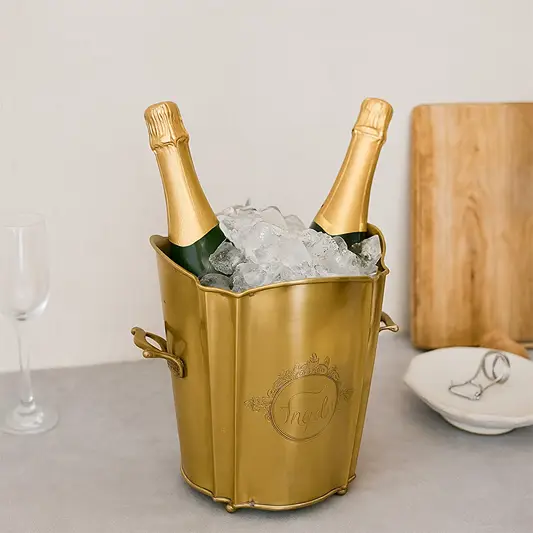 legant gold brass ice bucket with scalloped rim holding two champagne bottles and ice cubes on a modern table for party celebration.