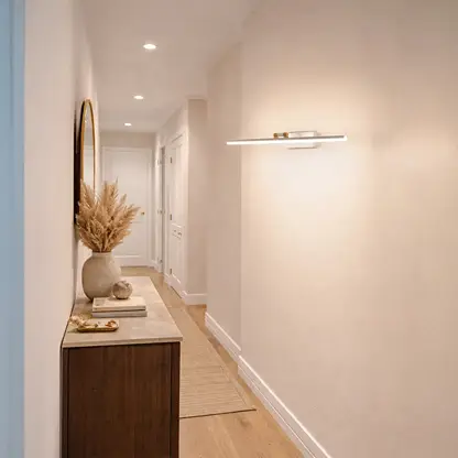 Gold metal picture light enhancing hallway artwork with warm illumination creating sophisticated interior ambiance.