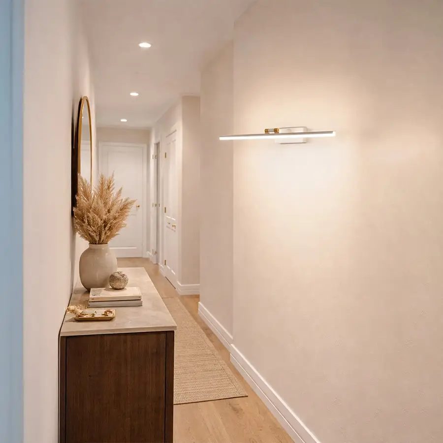 Gold metal picture light enhancing hallway artwork with warm illumination creating sophisticated interior ambiance.